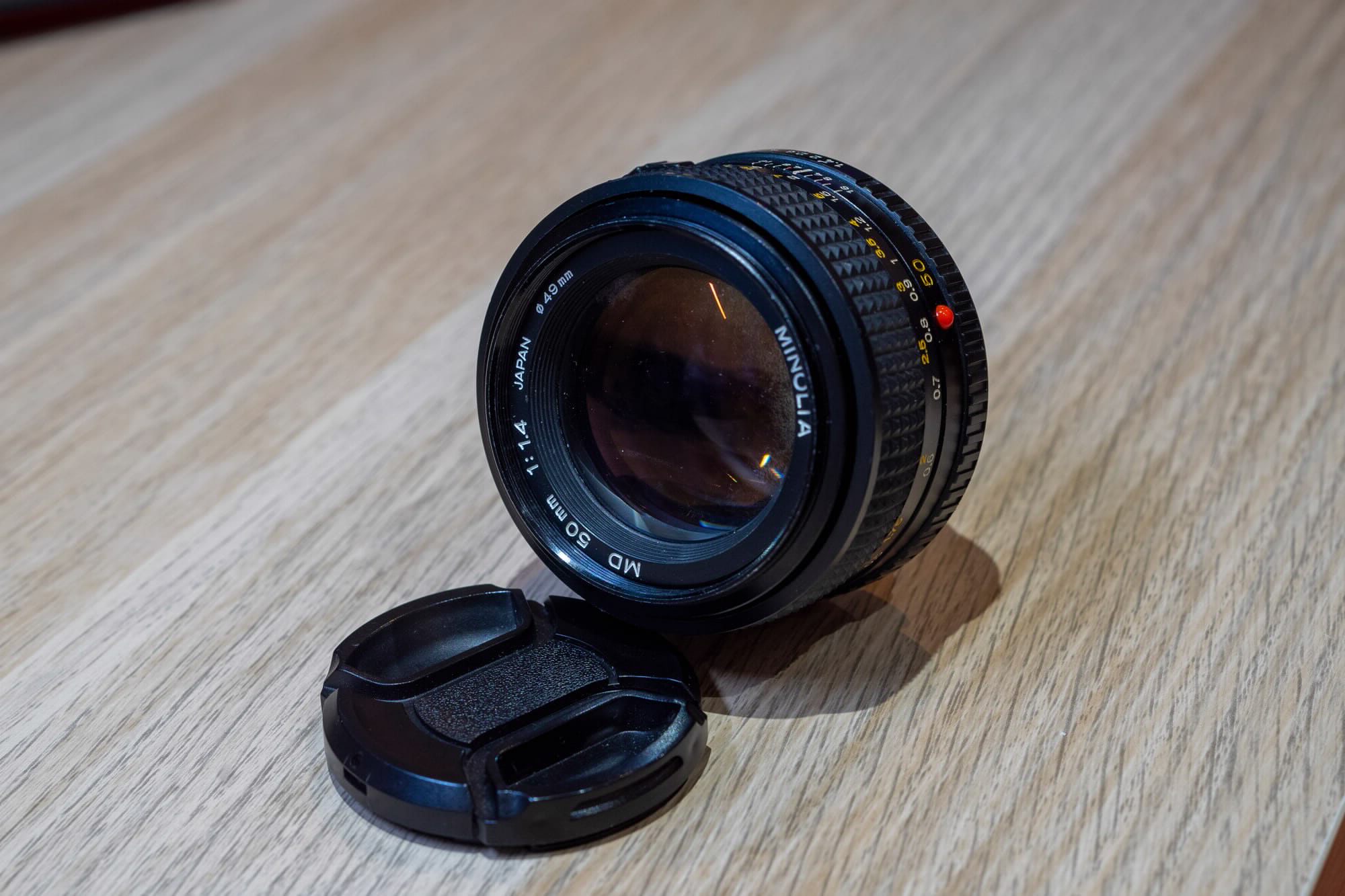 The Minolta MD 50mm f/1.4 resting on my desk with its lens cap next to it